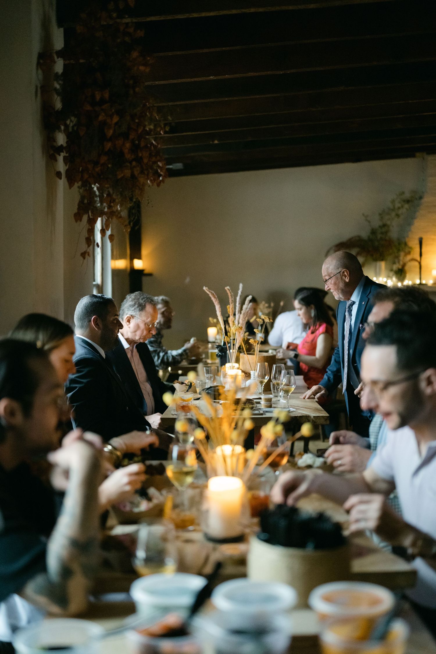 People gather around a dimly lit table for an intimate dinner party with candles and shared dishes at Fadensonnen in Baltimore
