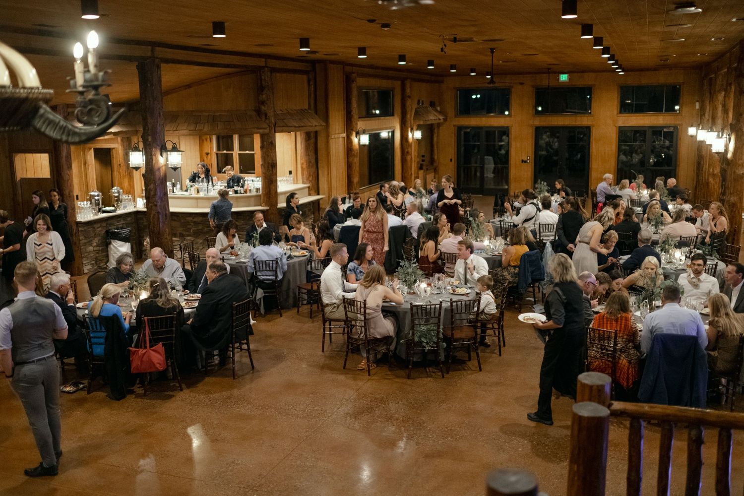 Large wedding reception in an elegant wooden ballroom with guests seated at round tables.