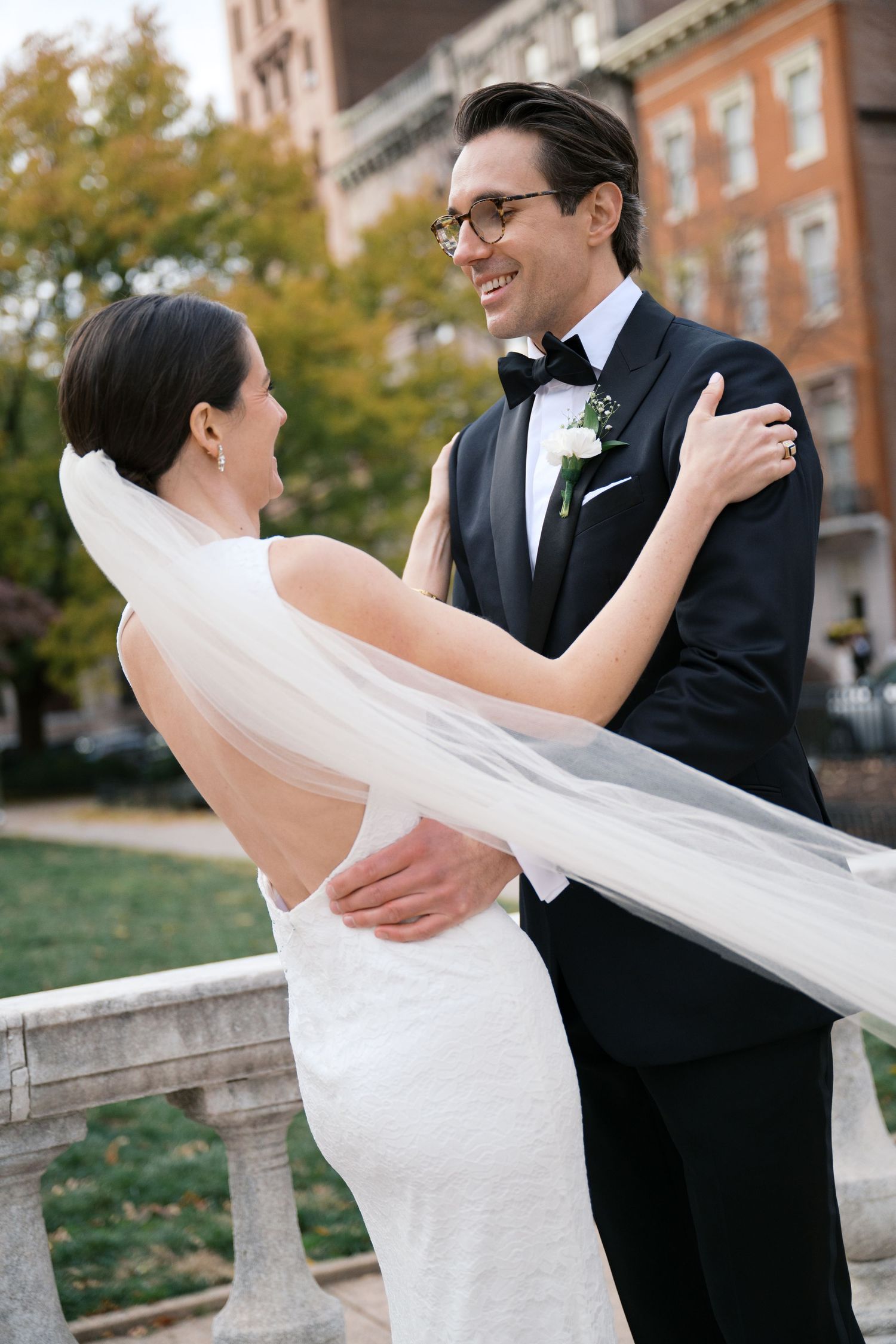Romantic wedding portrait with flowing veil and elegant attire against urban backdrop.