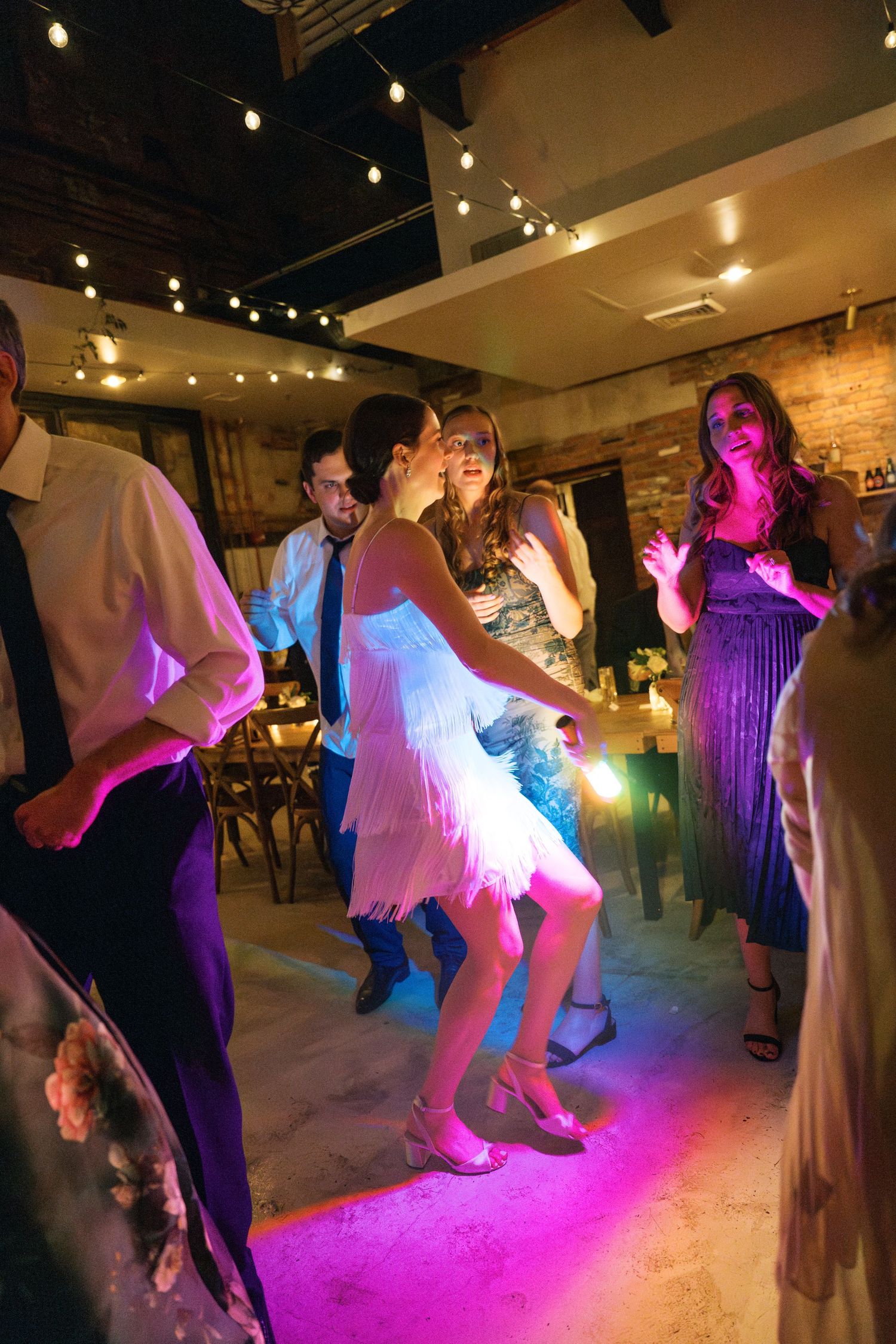 People dancing on a dance floor illuminated by colorful pink and blue lighting at an evening celebration.