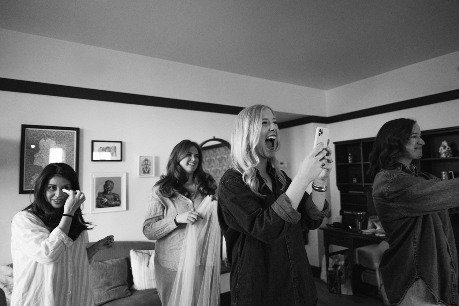 Black and white photo of wedding party members with raised hands celebrating in a decorated room.