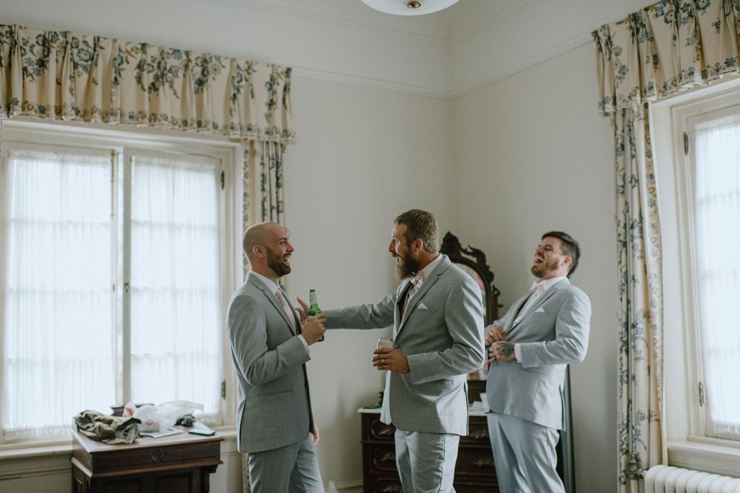 Groomsmen in matching gray suits helping each other prepare before the ceremony.