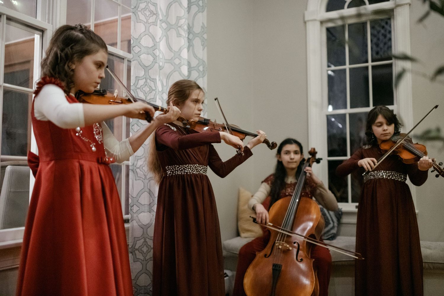 String quartet performers in red and burgundy dresses playing classical instruments.