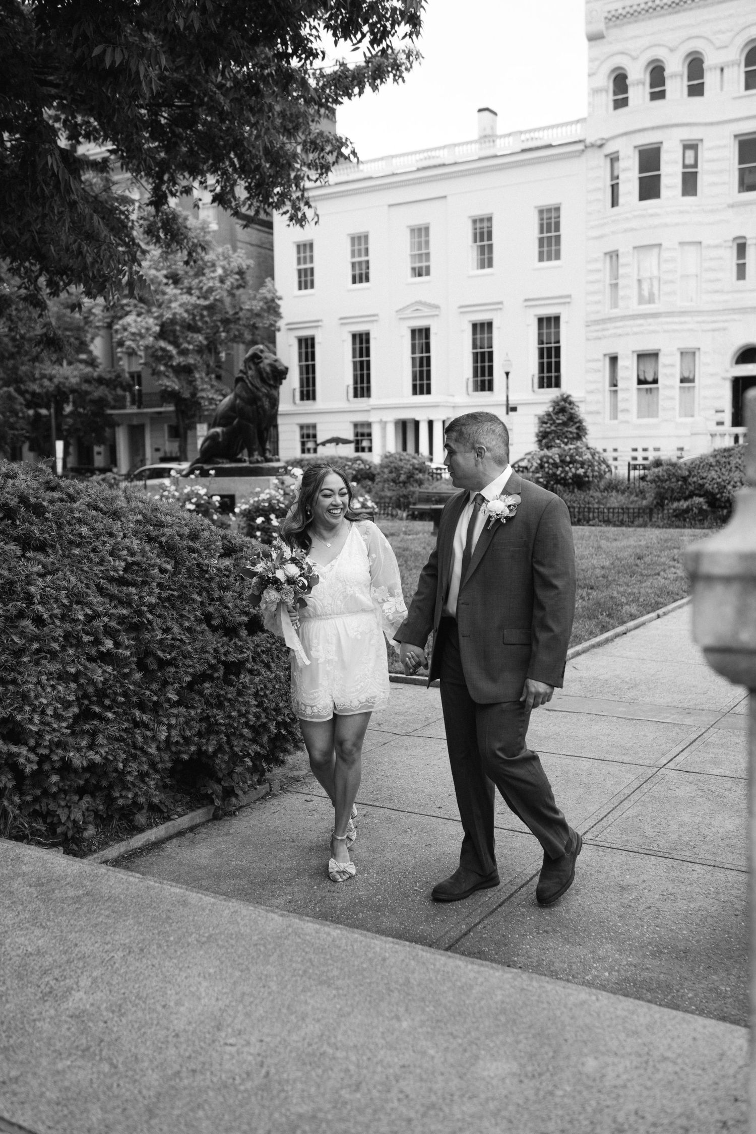 A couple walks together outside a grand white building during their wedding day celebration.