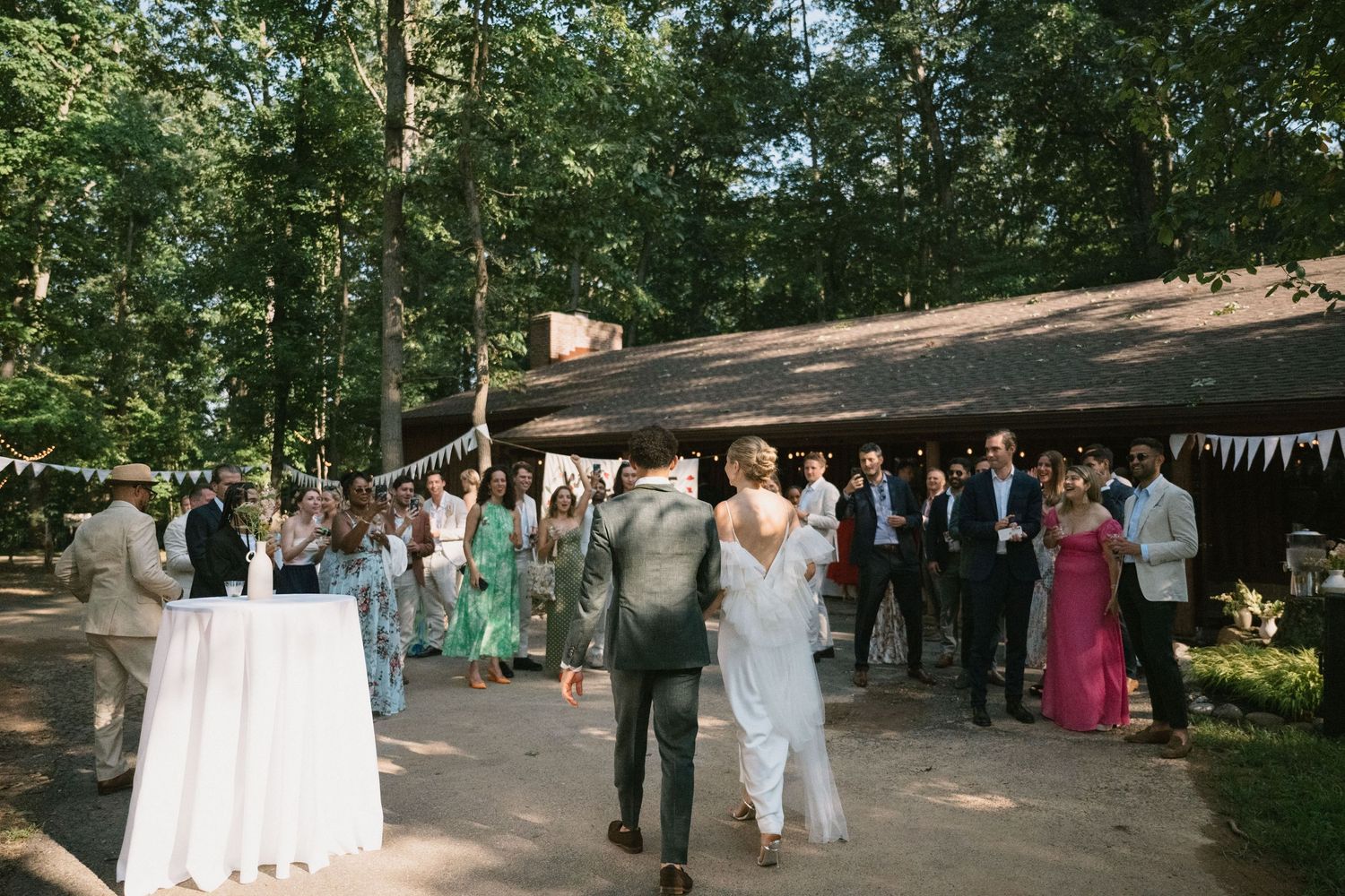 Wedding guests gather under a covered outdoor area decorated with white bunting.