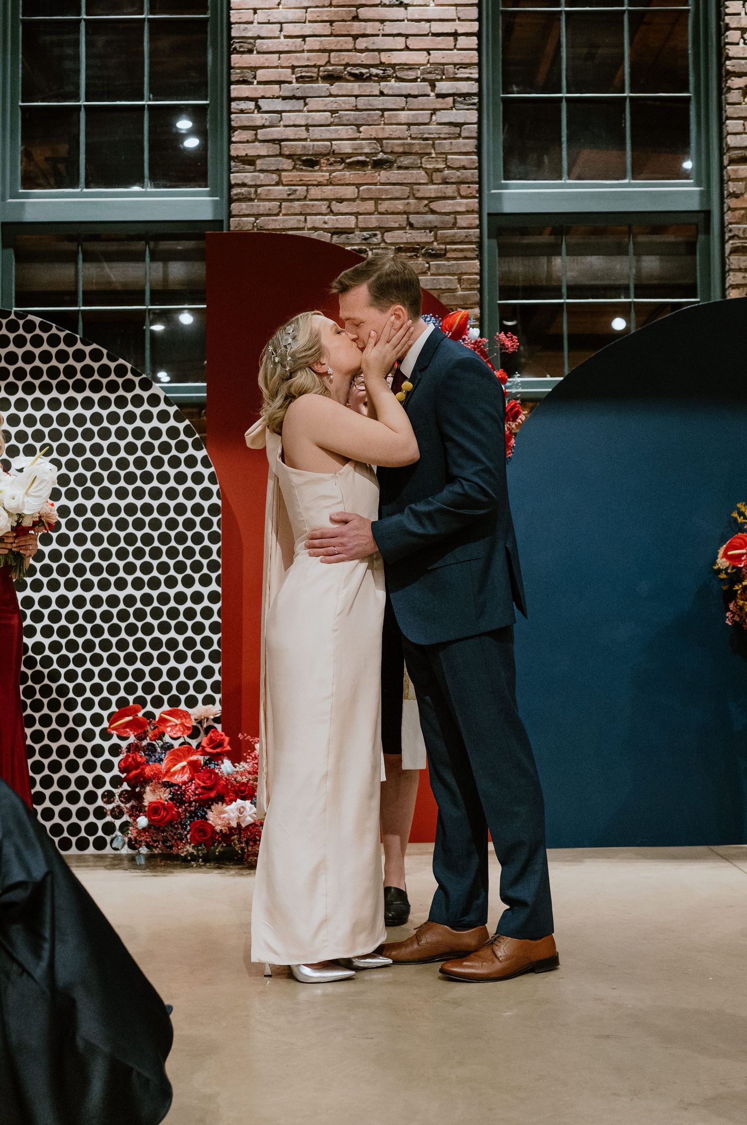 A tender moment between newlyweds in front of a modern backdrop with red flowers and navy panels.