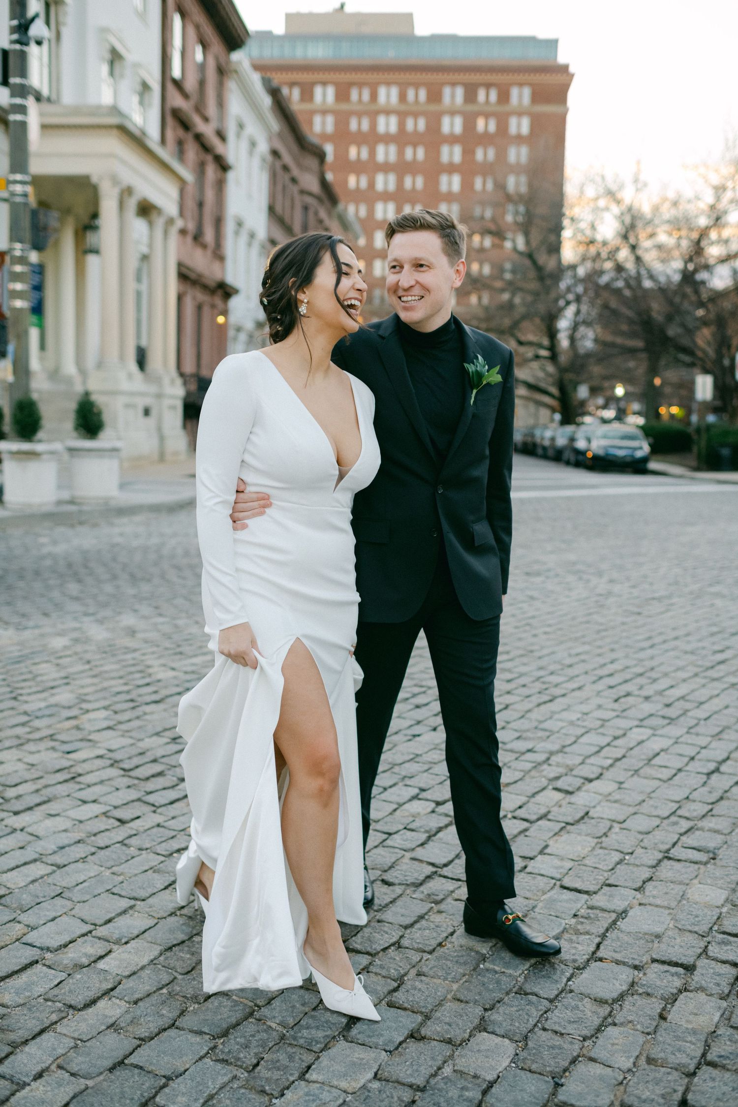 Wedding couple sharing happy moment on cobblestone street in urban setting.