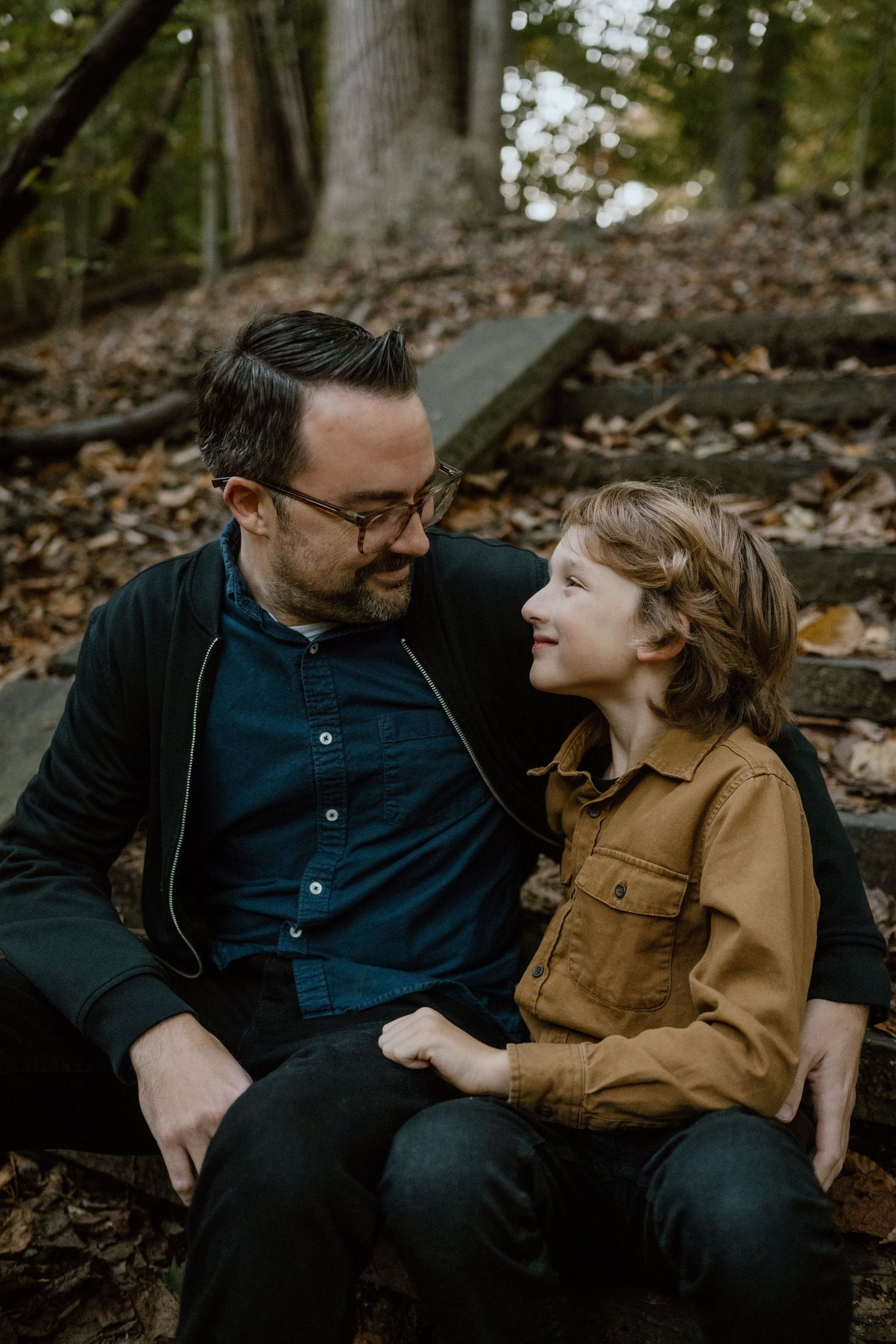 Two people share a special moment together while sitting on fallen leaves in the woods.