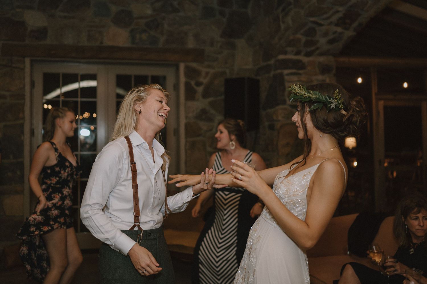 Wedding party members dance and celebrate in a rustic stone venue with dim lighting.