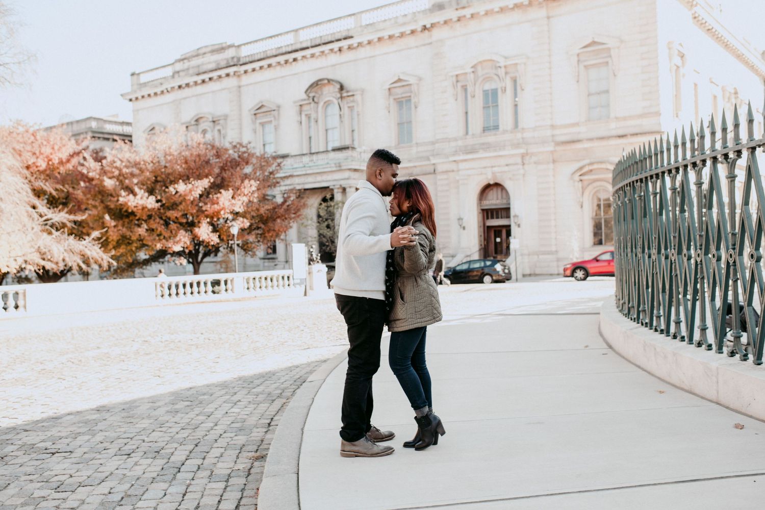 A couple standing close together on a cobblestone path near an elegant building.