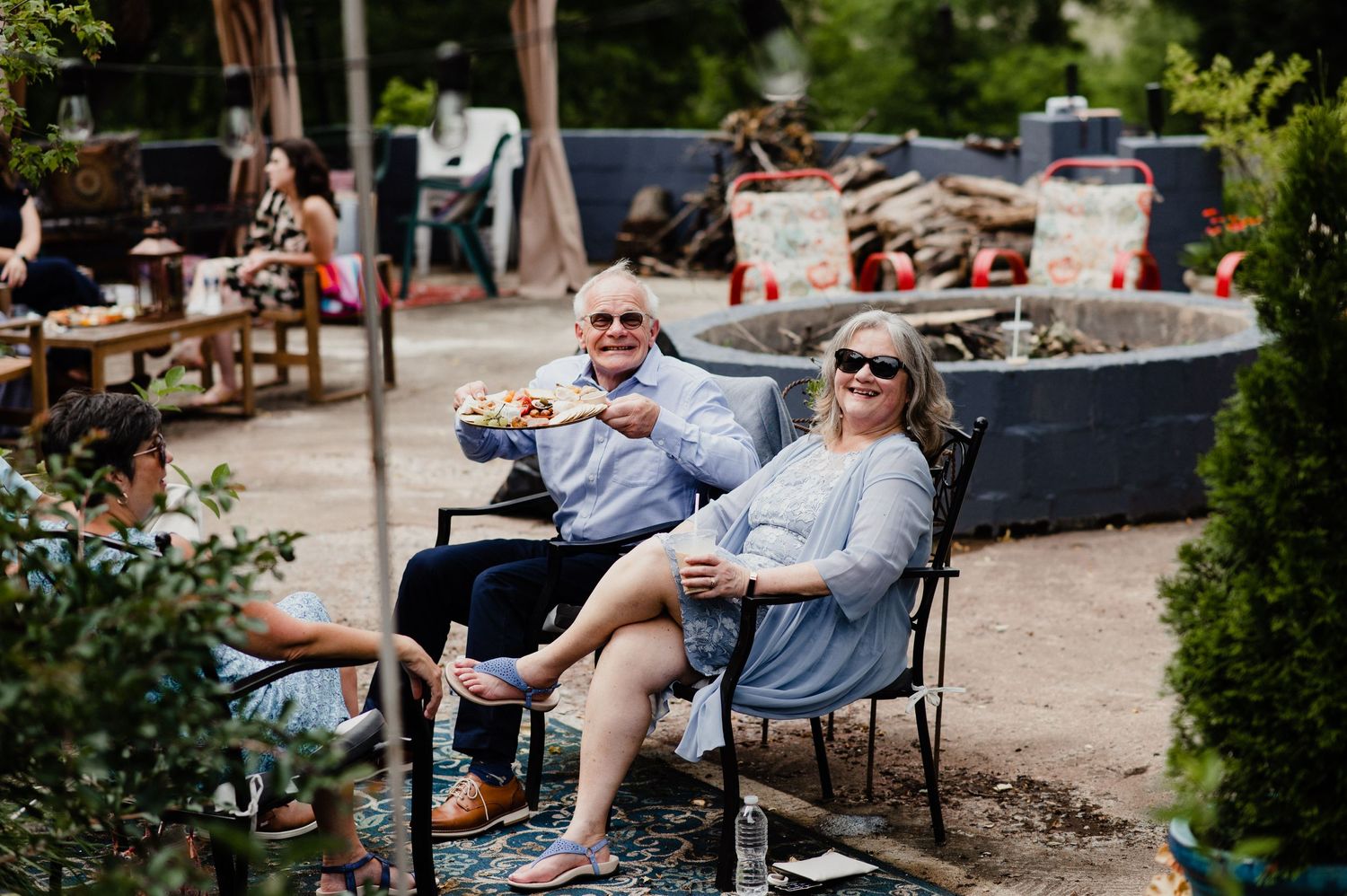 Two guests relax in outdoor chairs at a casual backyard gathering.