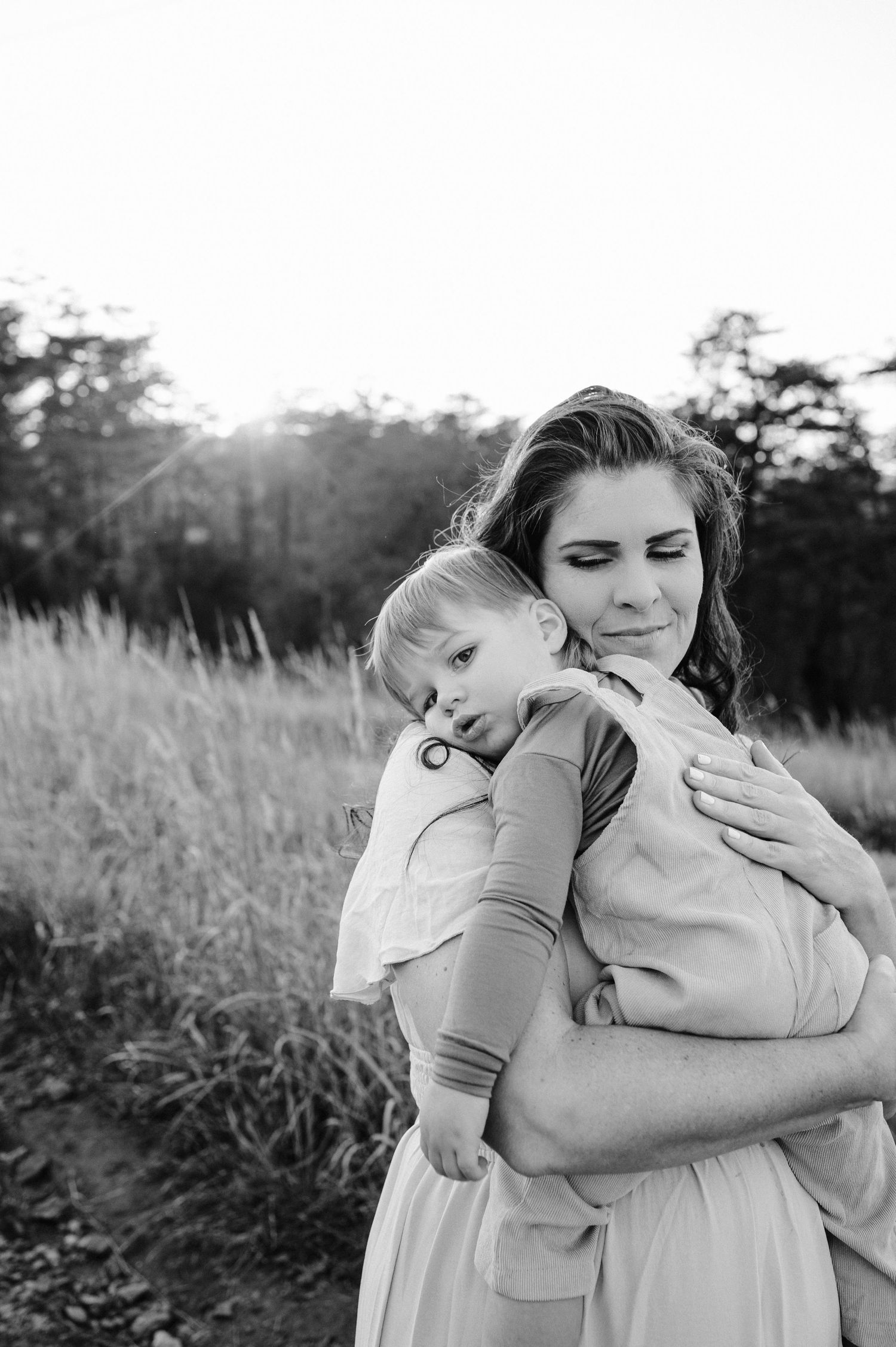 Black and white candid shot of a tender embrace in an outdoor setting with tall grass.