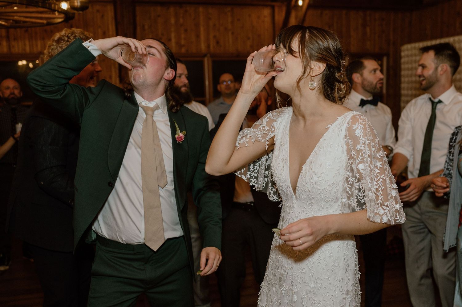 Wedding guests taking celebratory shots together at a rustic indoor reception.