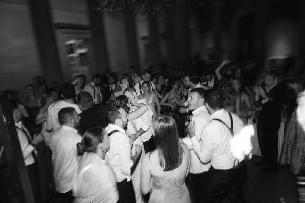 Black and white photo of crowd dancing with hands raised at nighttime party or celebration.