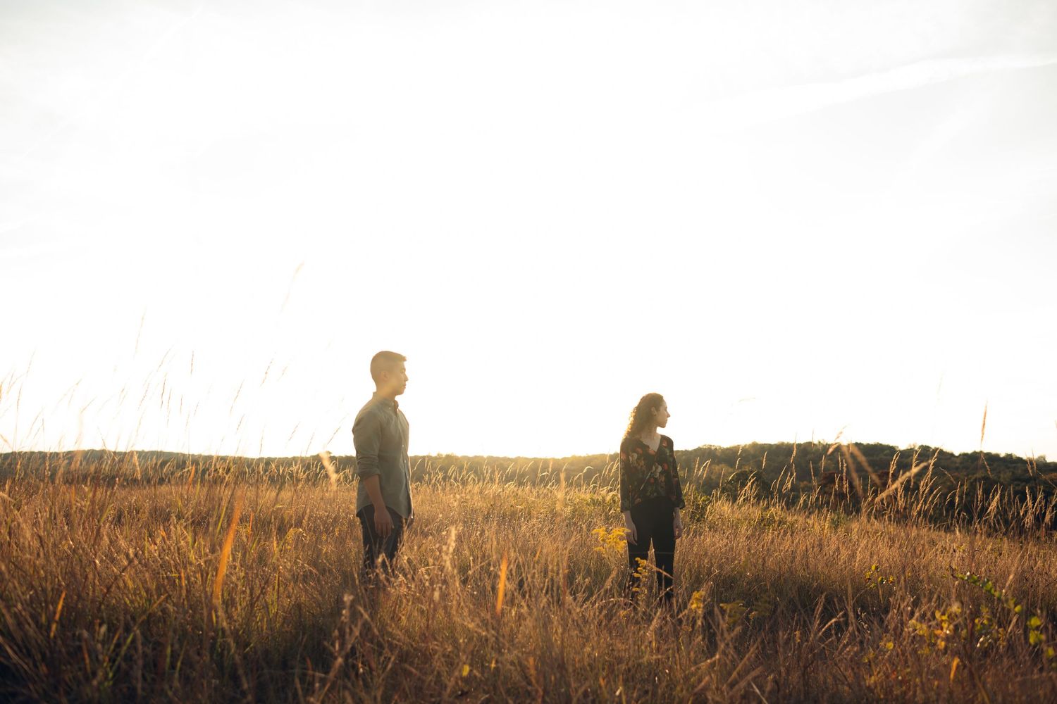 Distant view of couple standing in golden prairie grass at sunset.