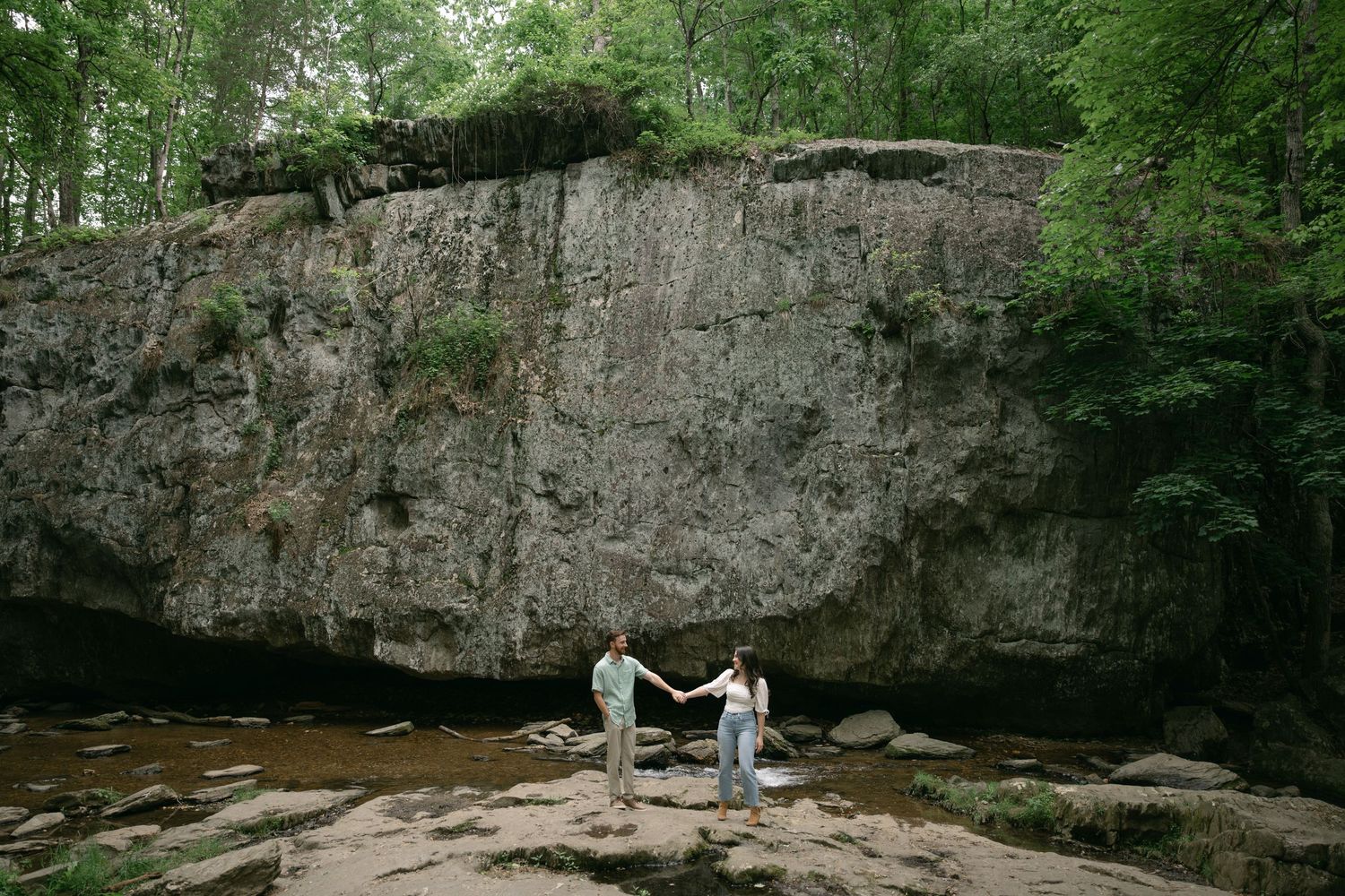 Natural rock formation and cliff face in a wooded area with stream.