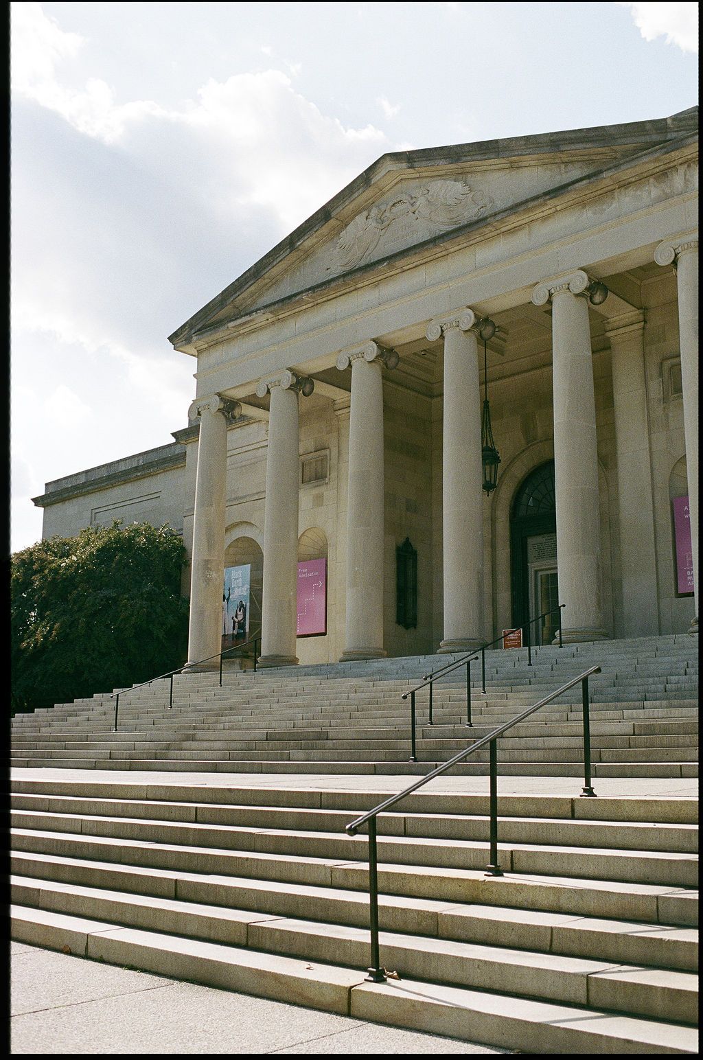 A series of wide stone steps lead up to a neoclassical building with white columns and triangular pediment.