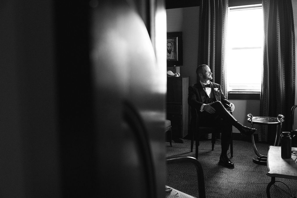 A dramatic black and white photograph shows a silhouetted figure standing in a dark room near a bright window.