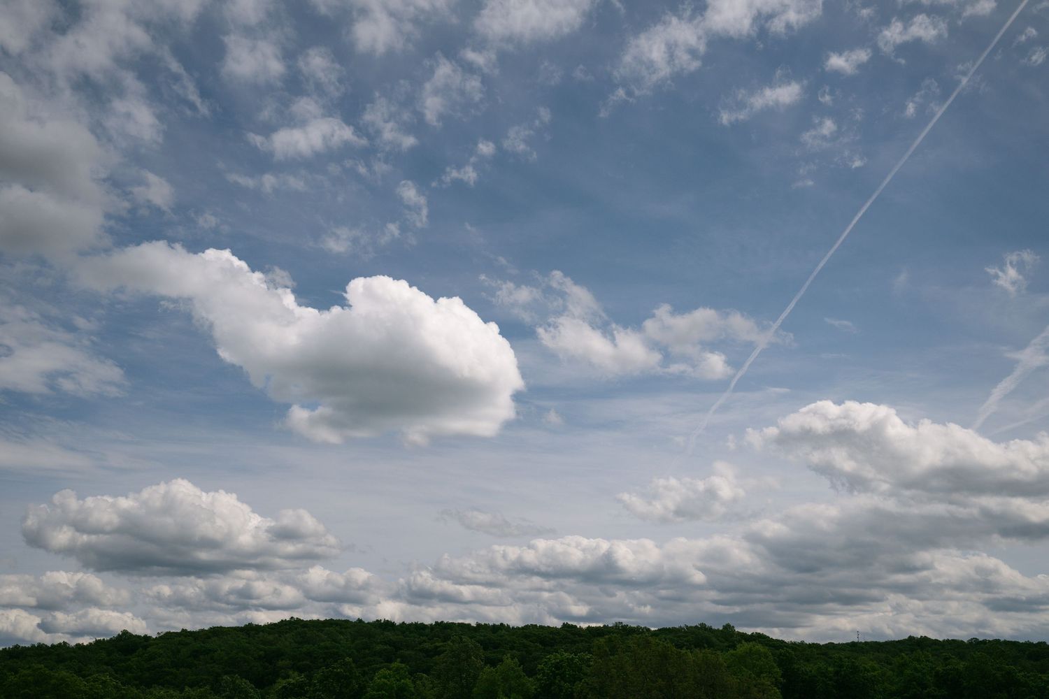 Panoramic view of rolling hills and puffy white clouds against a bright blue summer sky.