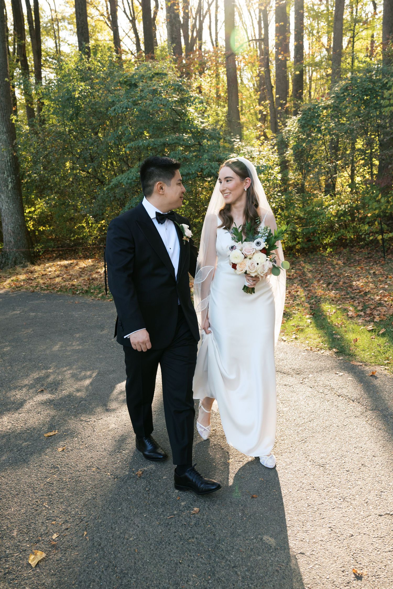 Wedding couple walking along a sunlit forest path during an autumn ceremony.