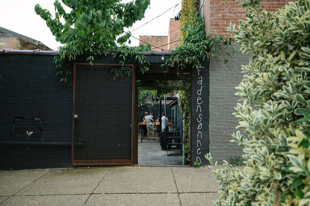 Green leafy trees and bushes frame an urban storefront entrance.