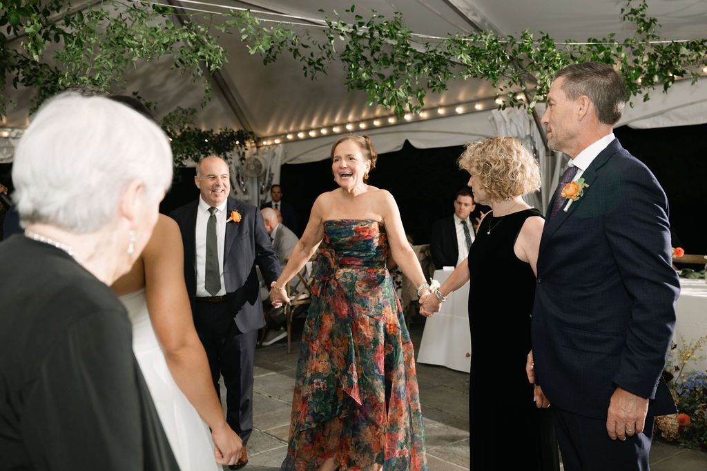 Guests enjoying a lively moment during an outdoor tented celebration with greenery decor.
