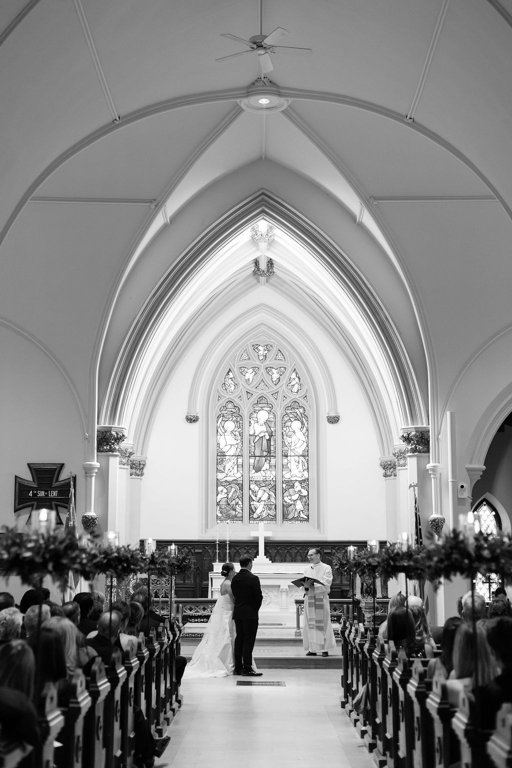 Black and white photo of a church wedding ceremony showing the long center aisle and gothic architecture.