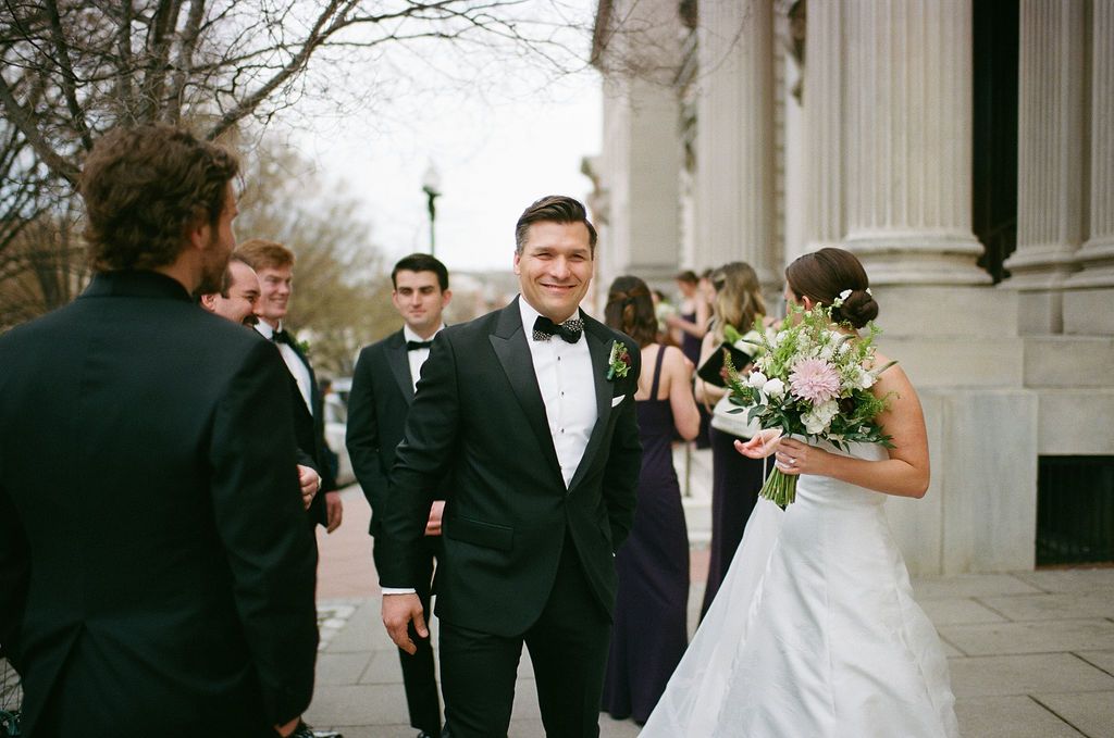 Wedding party poses on classical stone steps with white columns.
