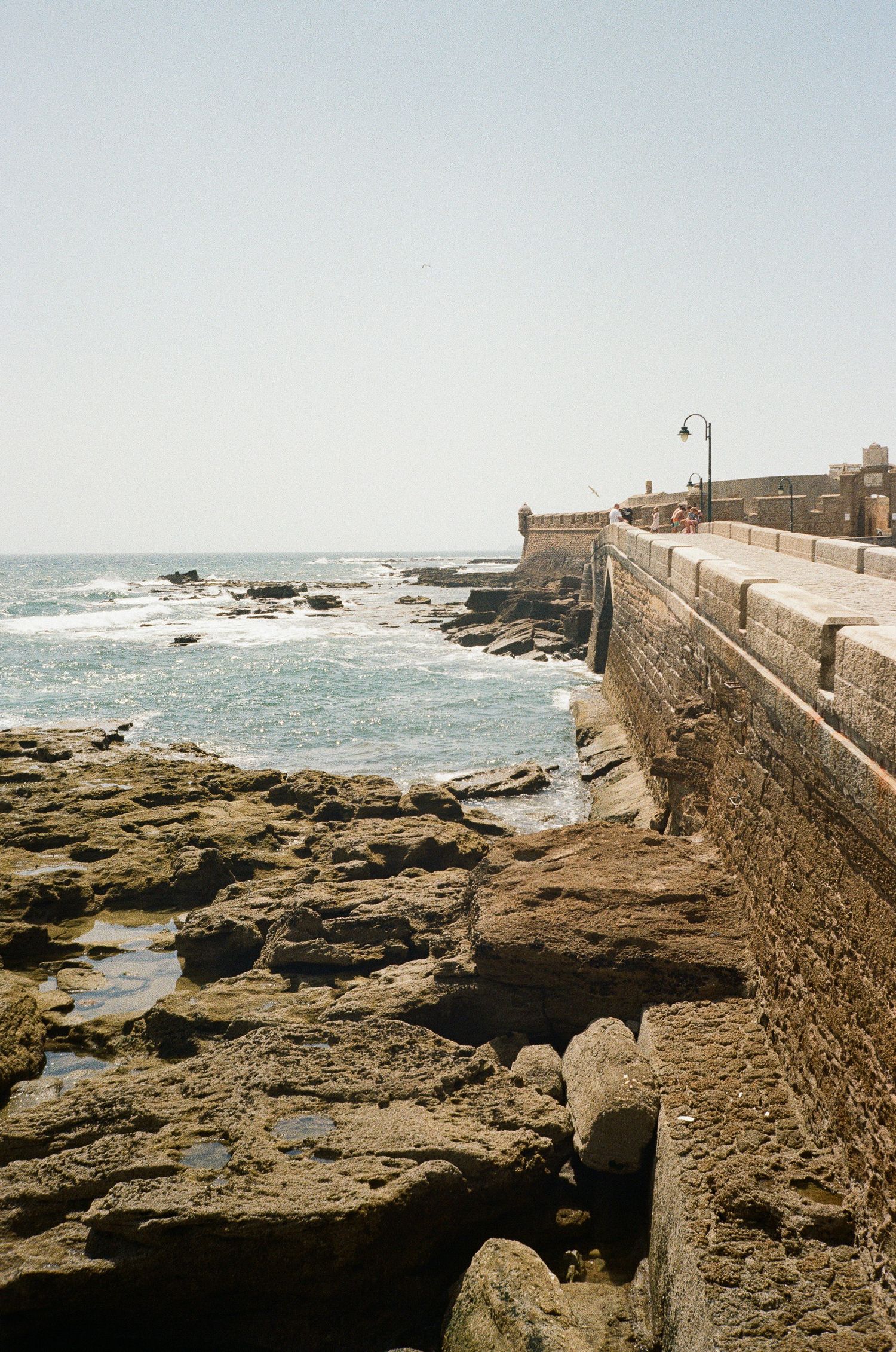 Rocky coastal shoreline with ancient stone fortress walls against crashing waves.