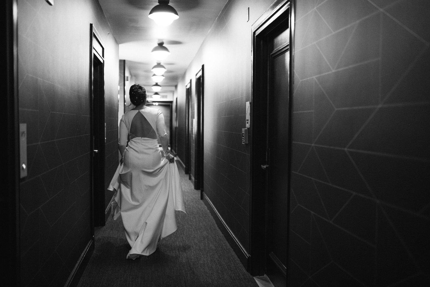 Dramatic black and white photo of bride walking down modern hotel hallway.