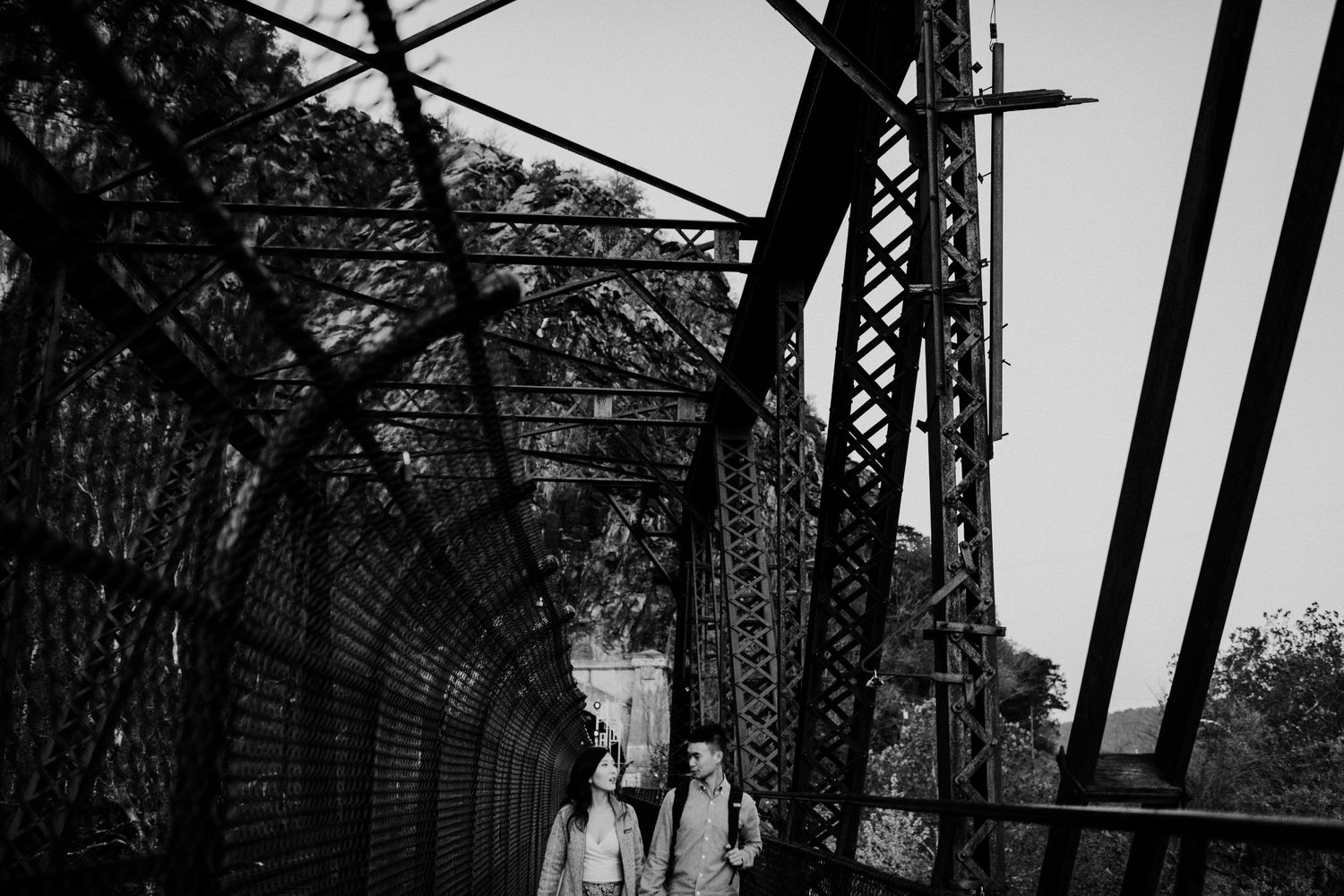 A couple walks through an industrial bridge structure in black and white.