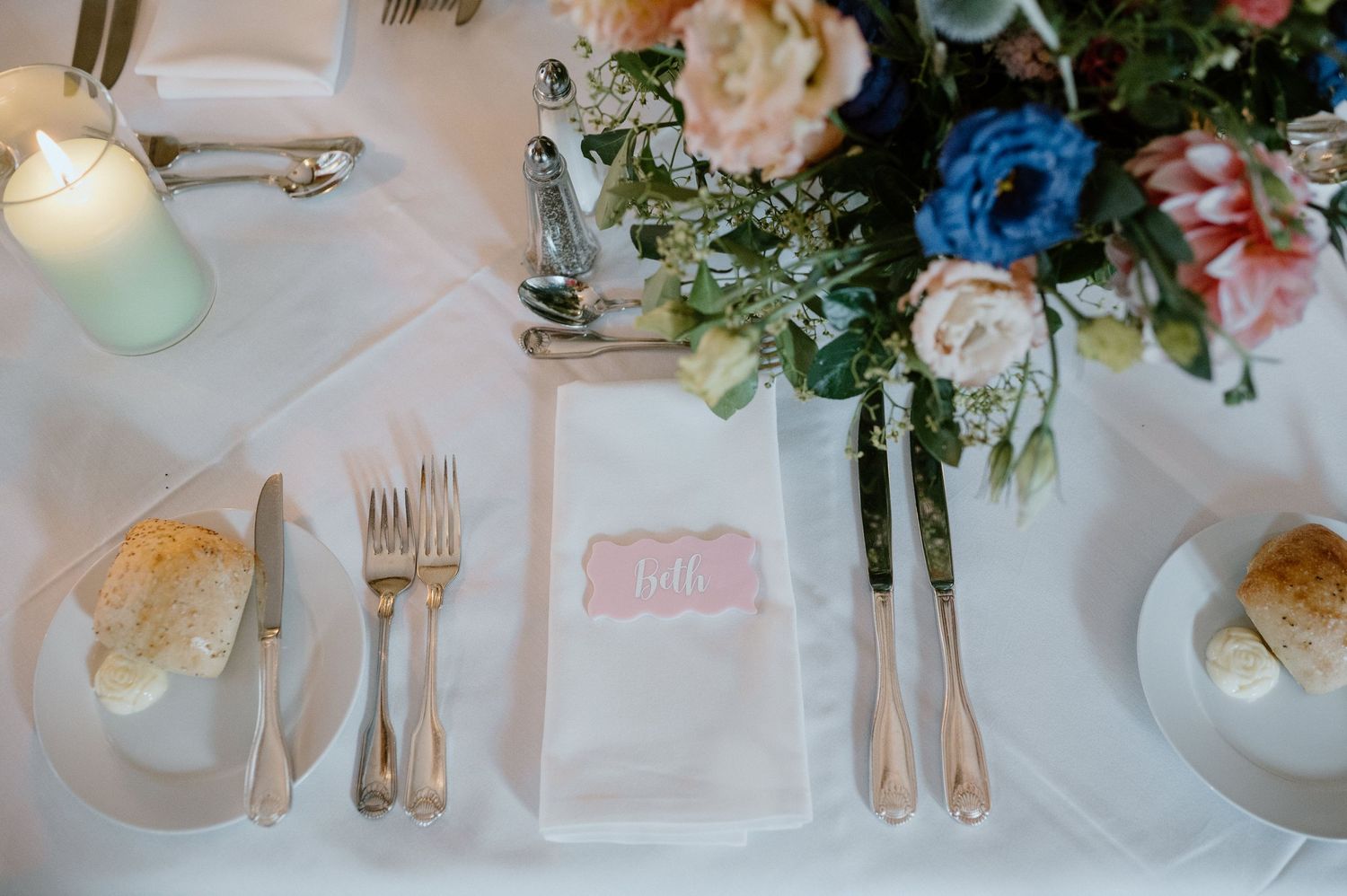 Close up of formal place setting with pink napkin and floral arrangement.