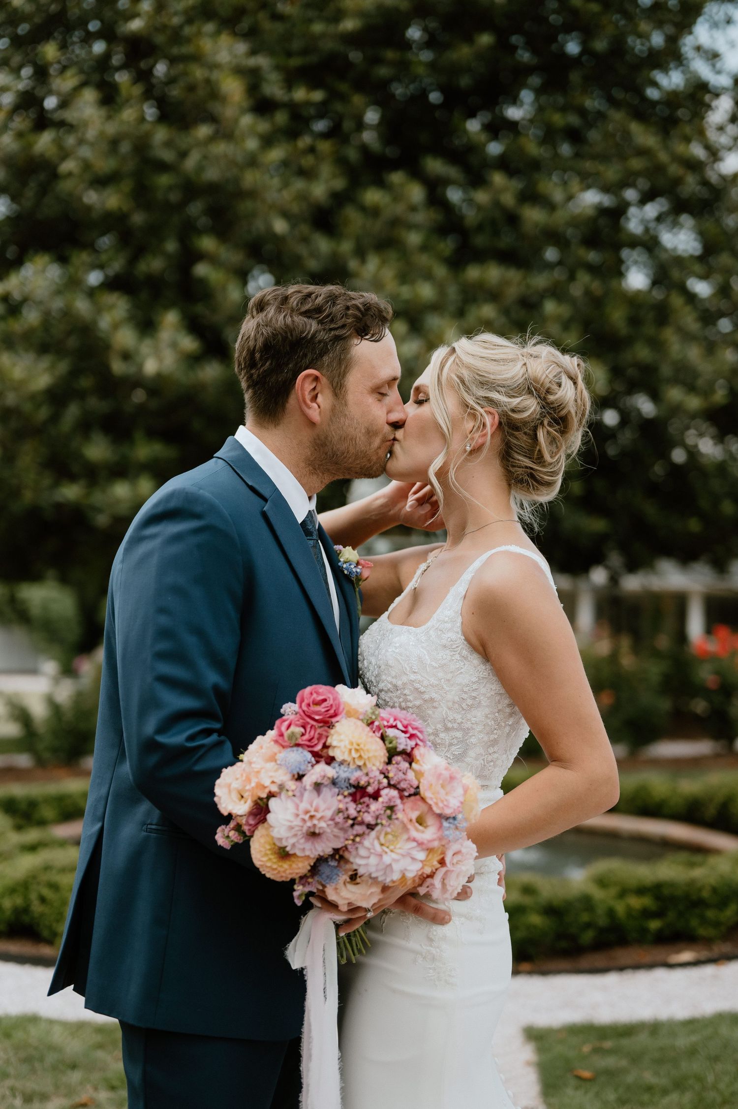 Romantic wedding moment captured in garden setting with pink and peach bouquet.