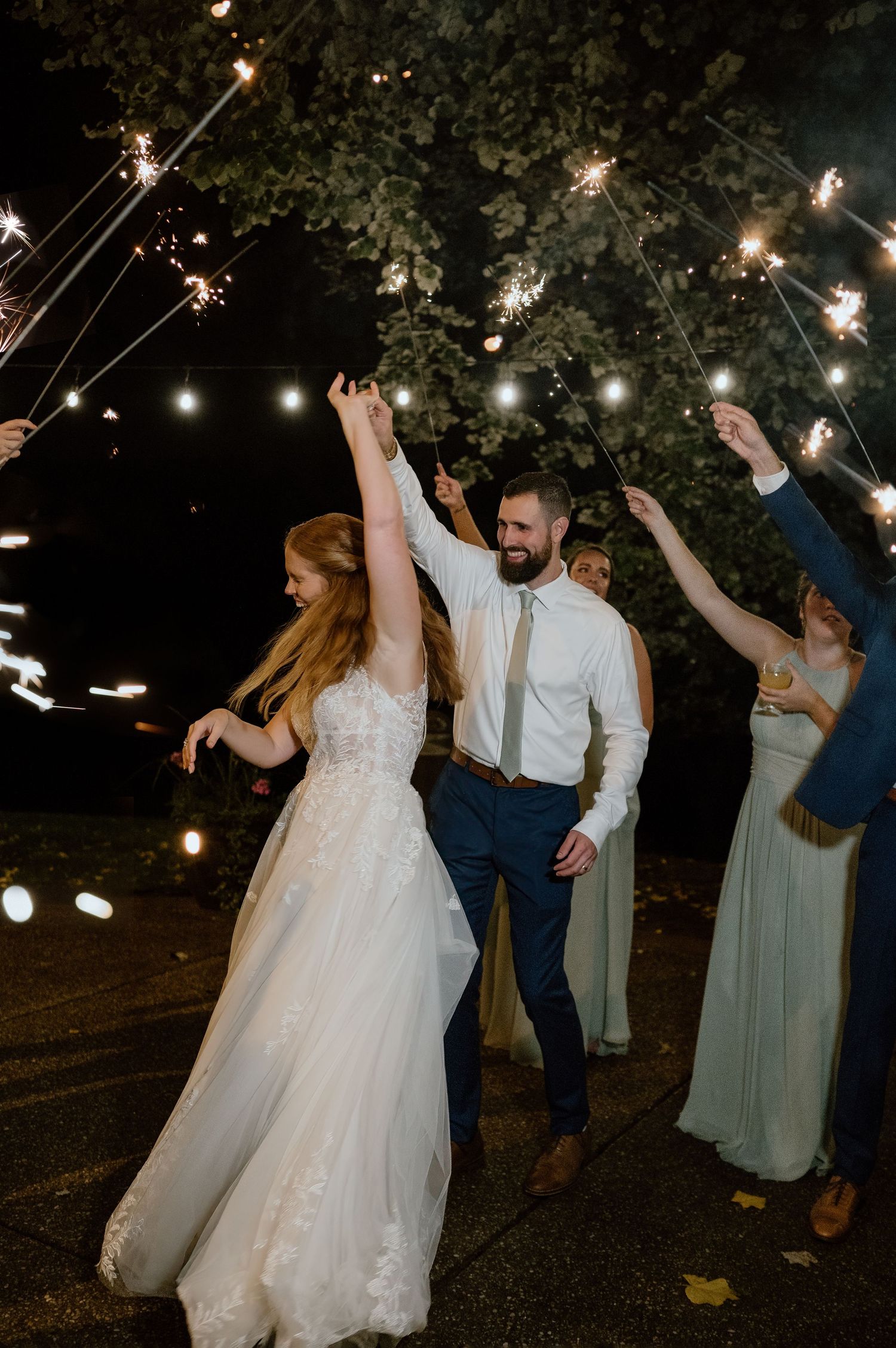 Wedding celebration under string lights with sparklers and guests dancing outdoors.