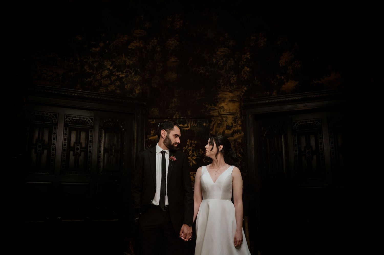 A dramatic low-light wedding portrait in a historic building with ornate wooden details.