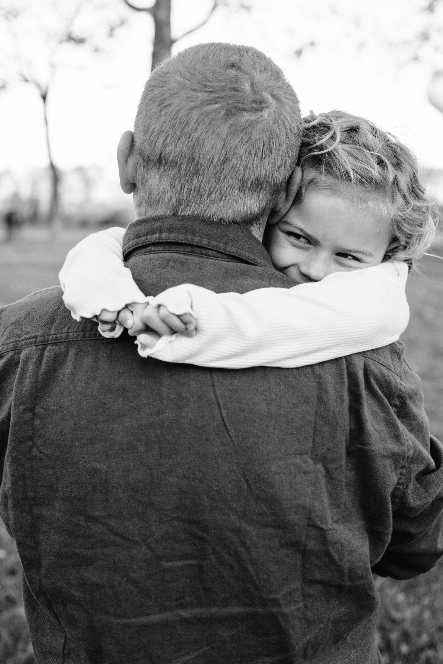 An intimate black and white moment captures a warm embrace against a natural background.