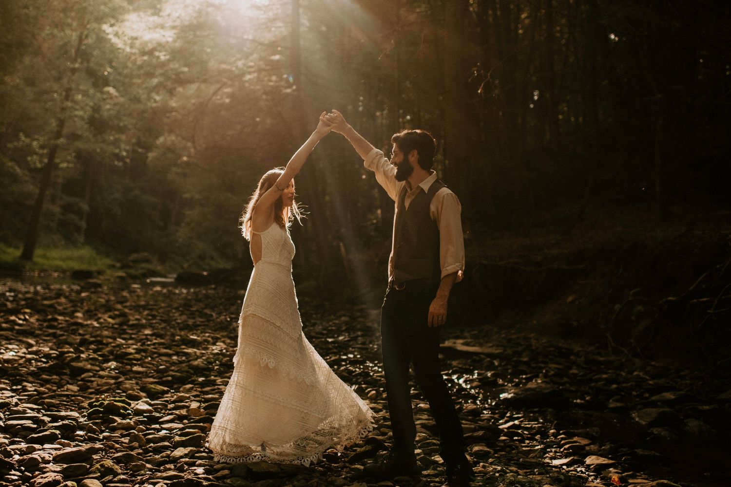 Couple dancing together in magical forest setting with dramatic backlighting.