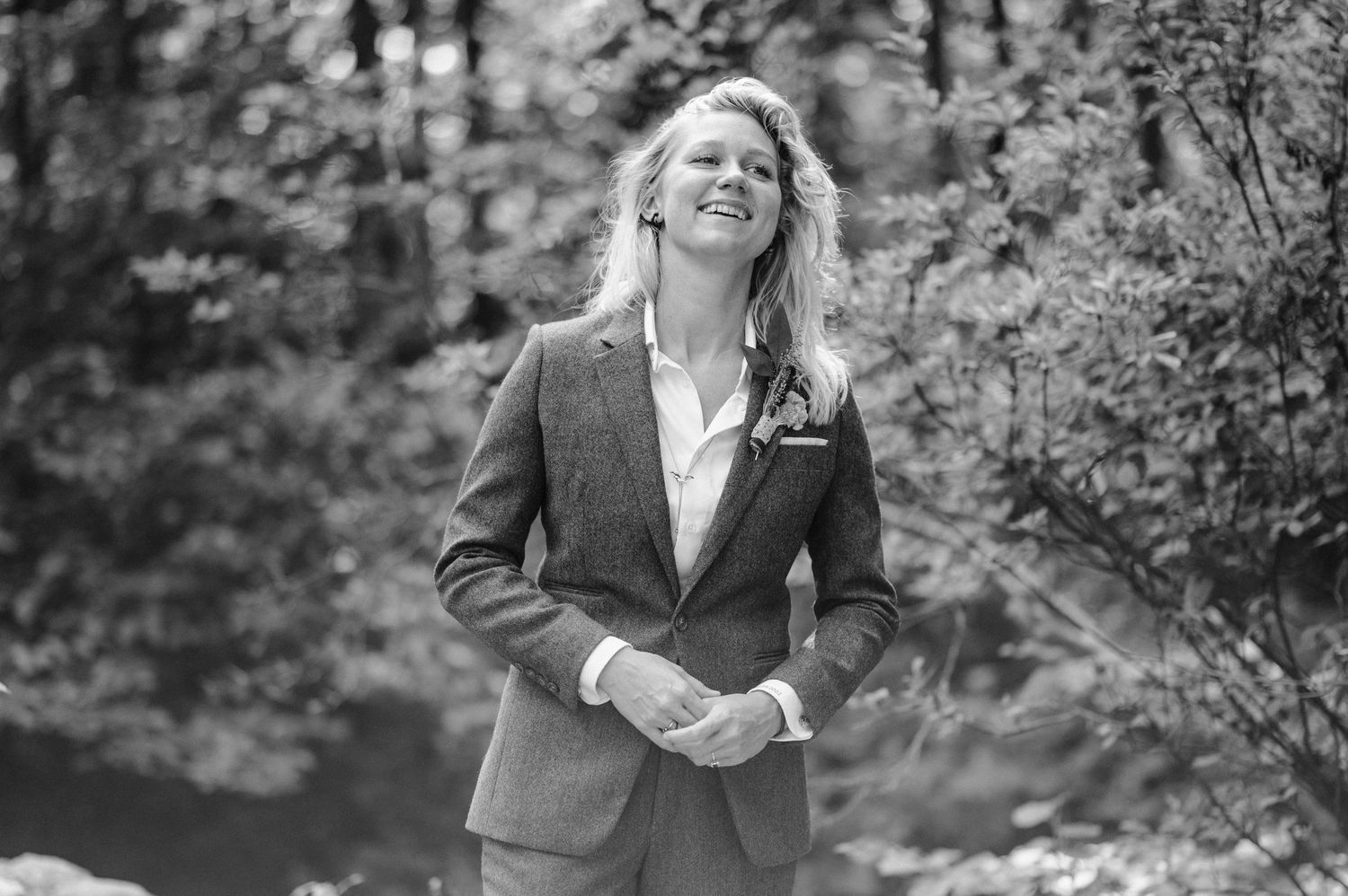Black and white portrait of person in formal attire outdoors among trees.