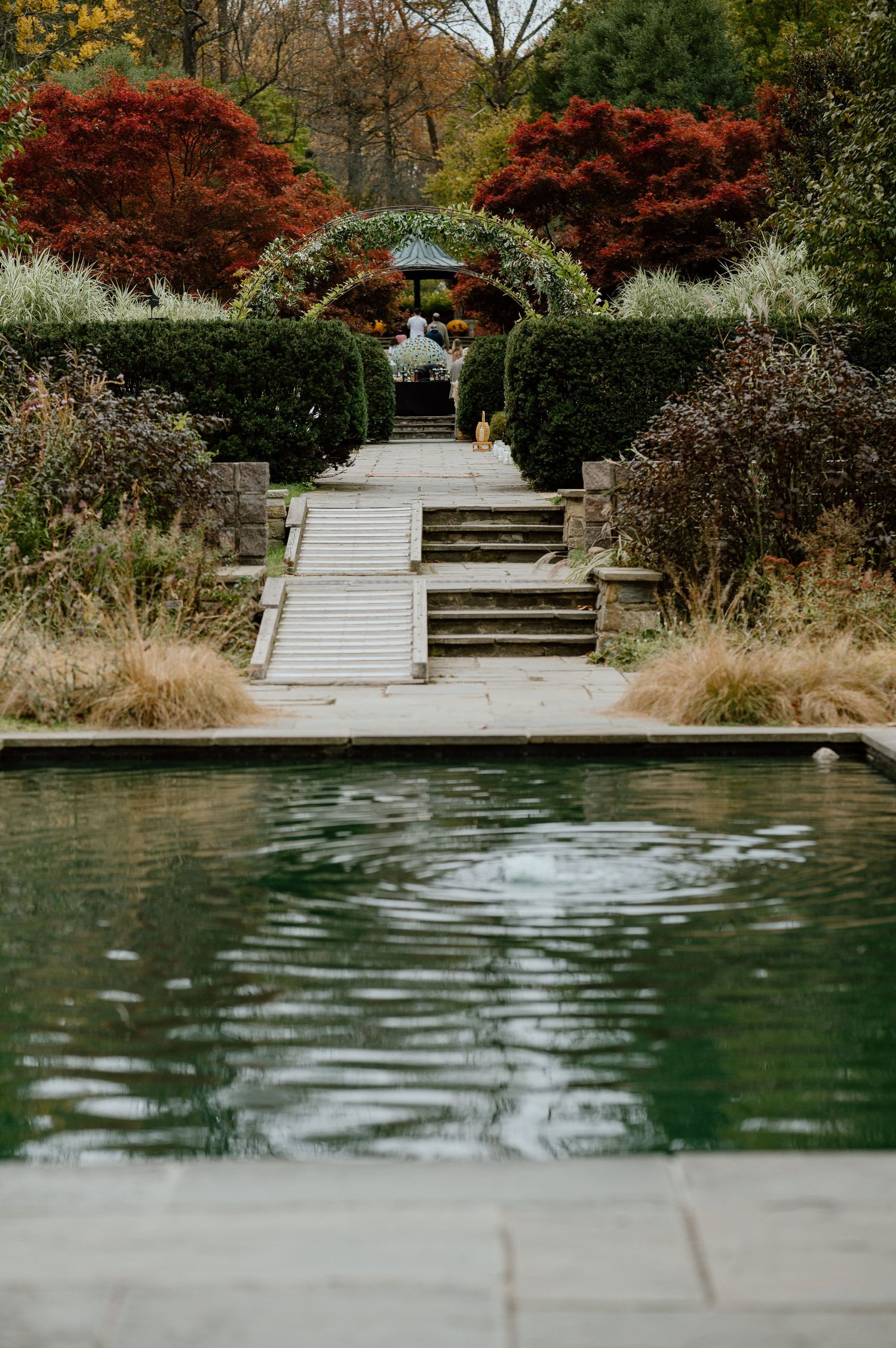 Elegant garden steps leading to a gazebo with red Japanese maples and reflecting pool in foreground.
