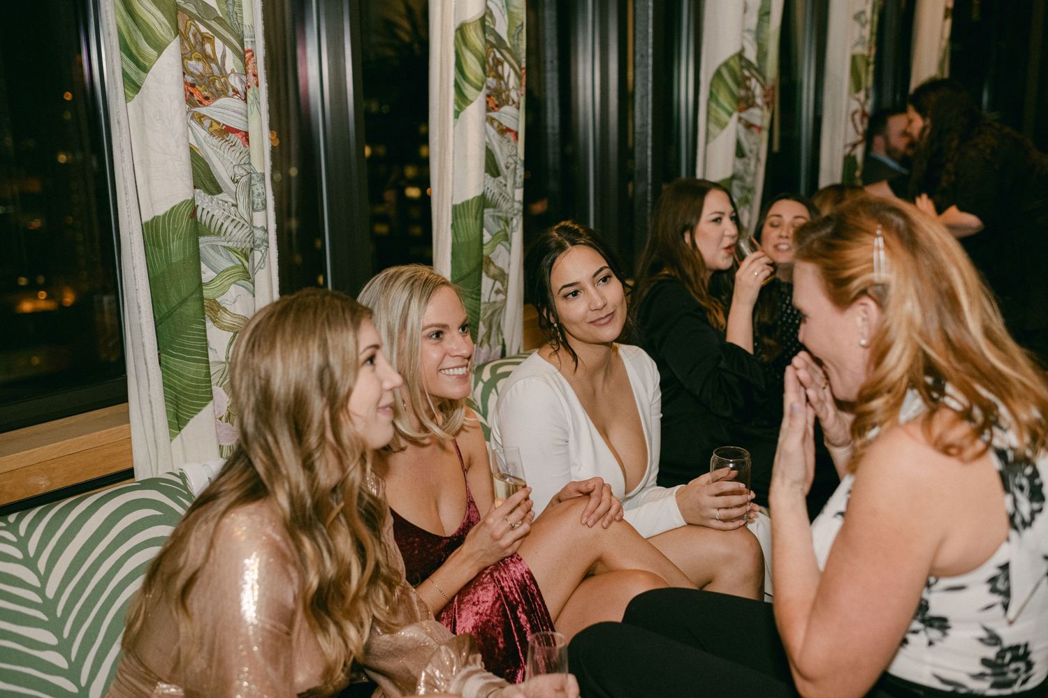 Wedding guests socializing on patterned upholstered seating at evening reception.