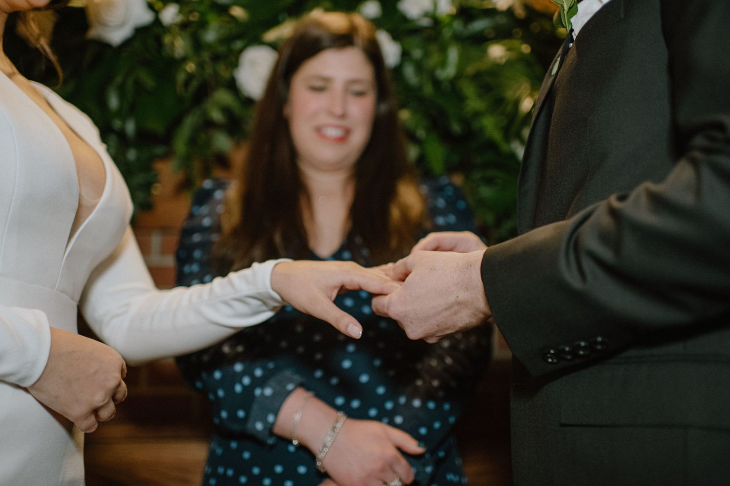 A close-up of hands exchanging rings during an indoor wedding ceremony.