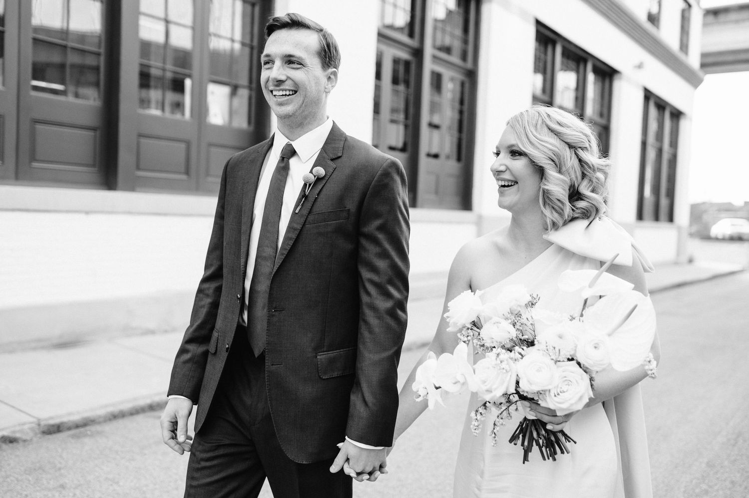 Black and white wedding portrait of couple smiling while walking outdoors.