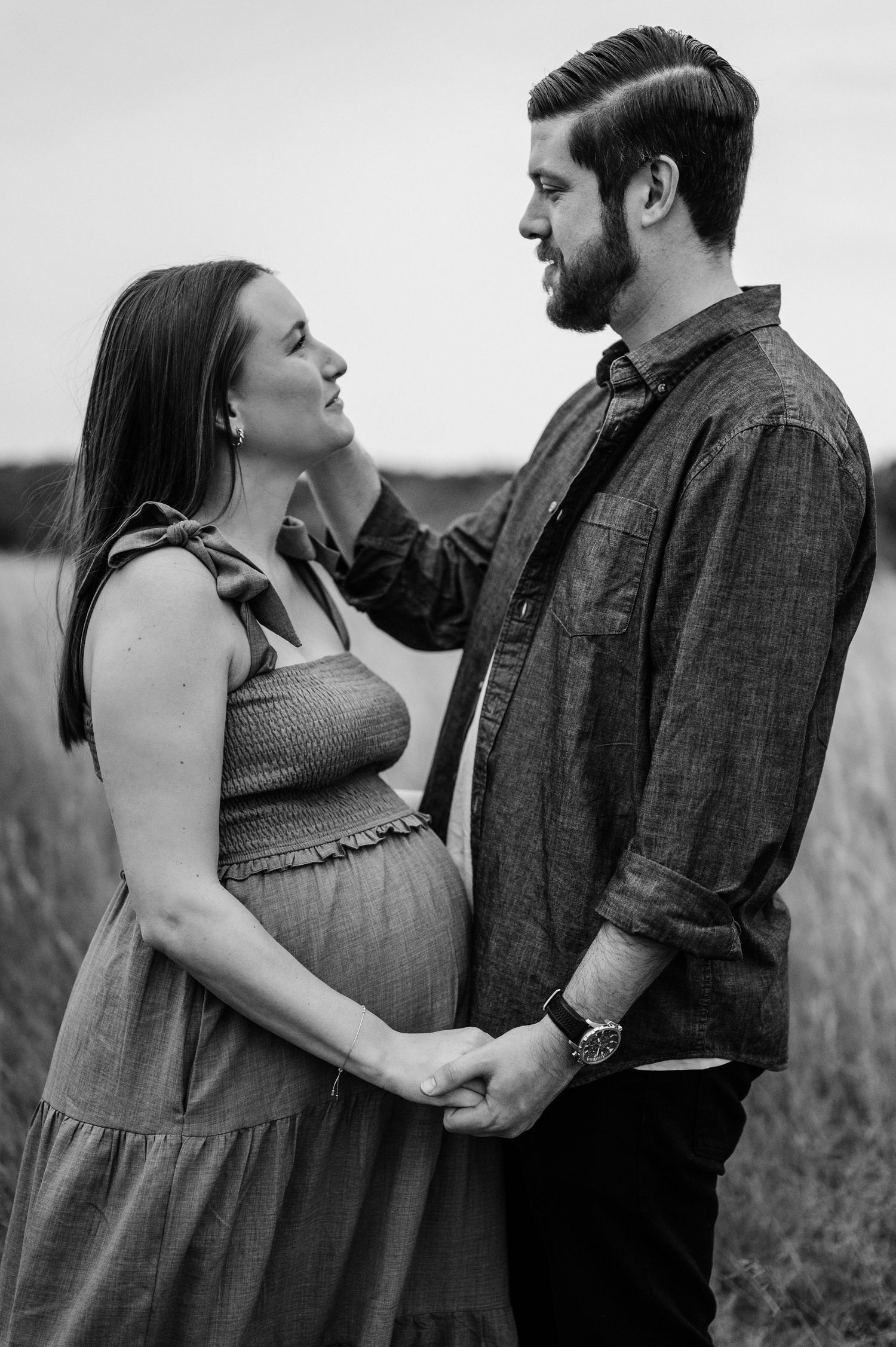 Black and white maternity portrait of couple tenderly embracing in field.