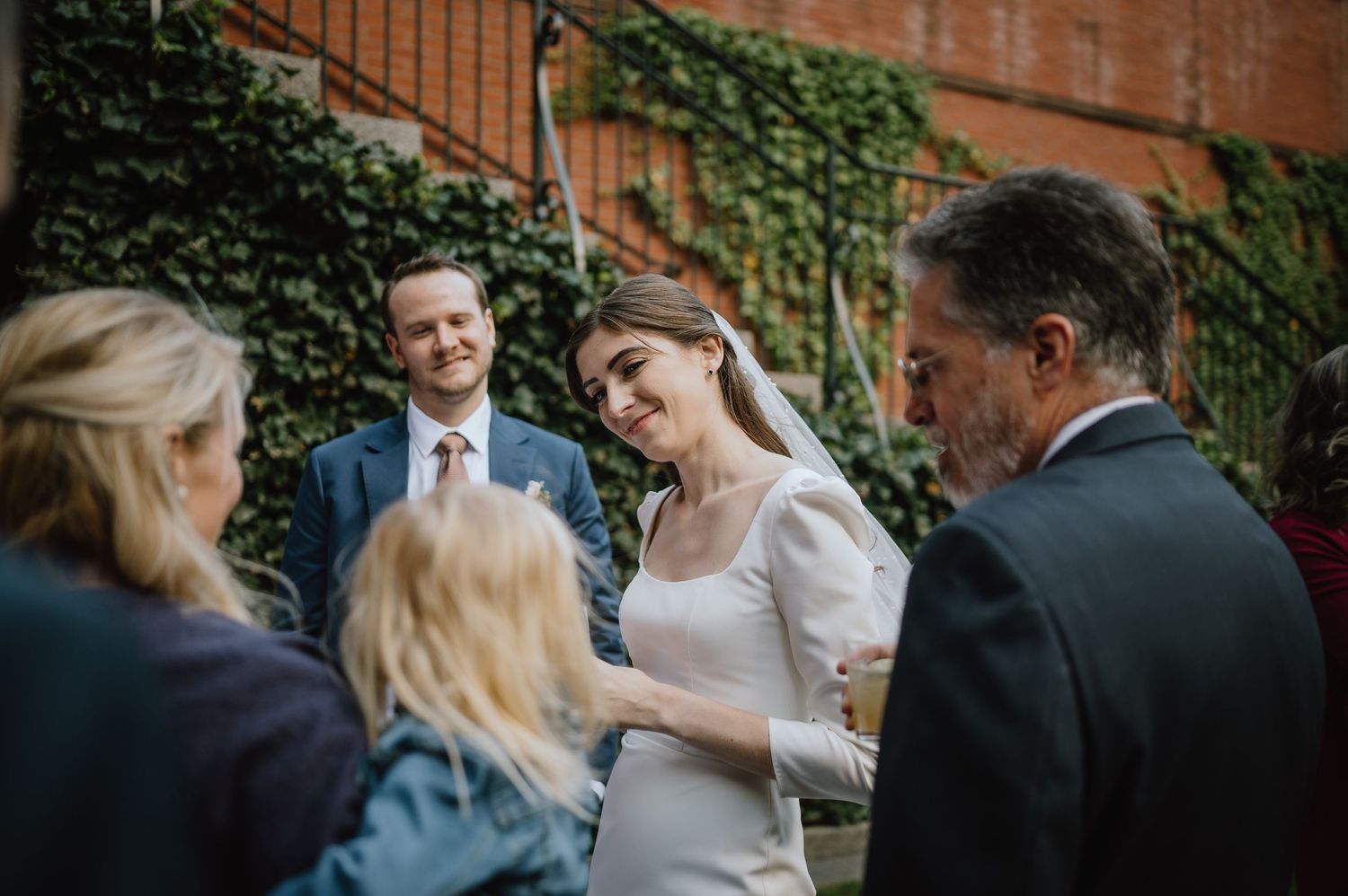 Wedding guests sharing joyful moments during an outdoor reception against an ivy wall backdrop.