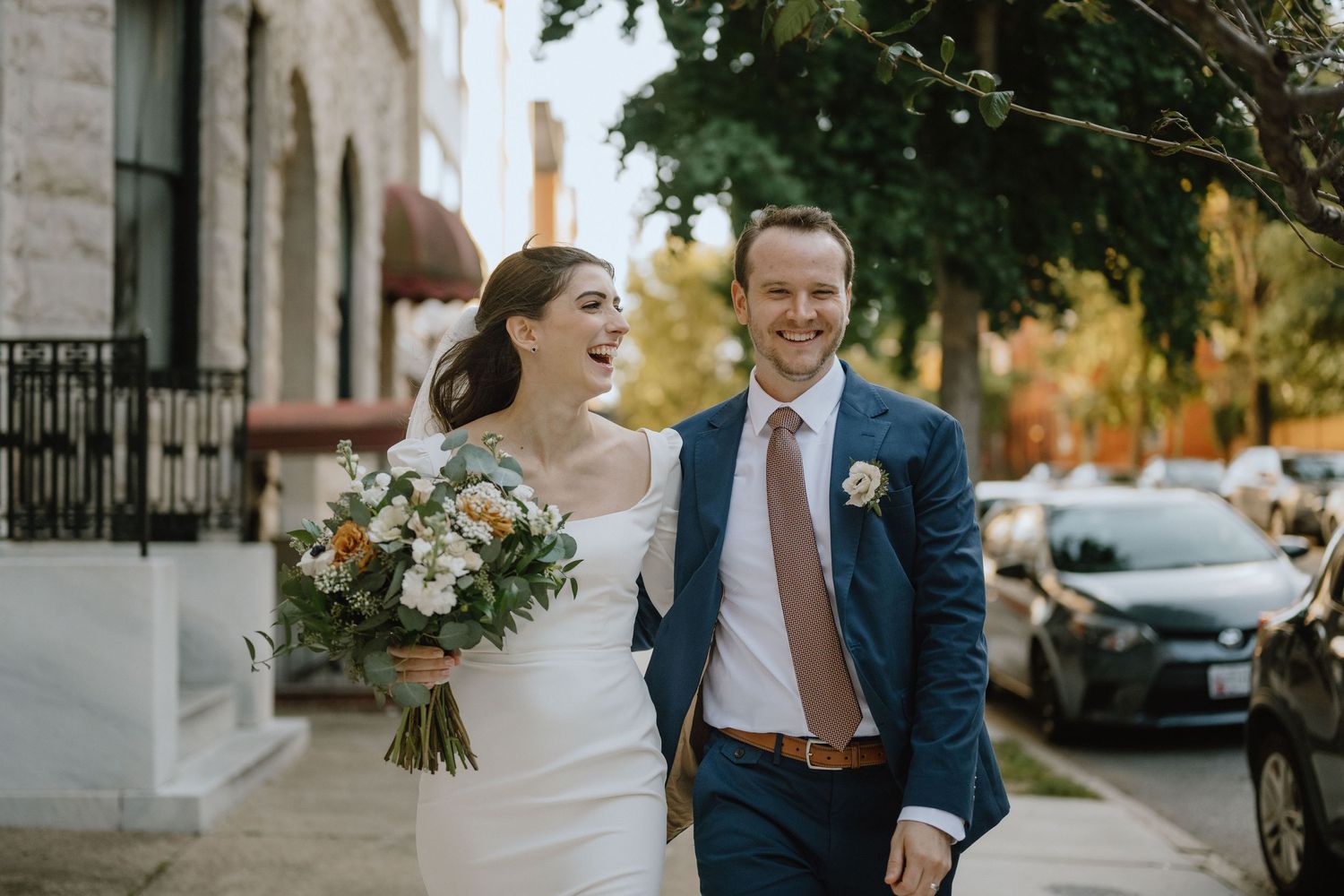 Candid wedding moment captured on a tree-lined street with beautiful natural lighting.