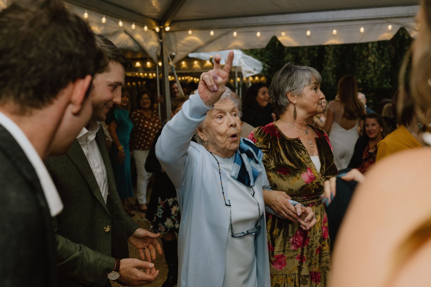 Guests dancing and celebrating at a lively outdoor wedding reception under string lights.