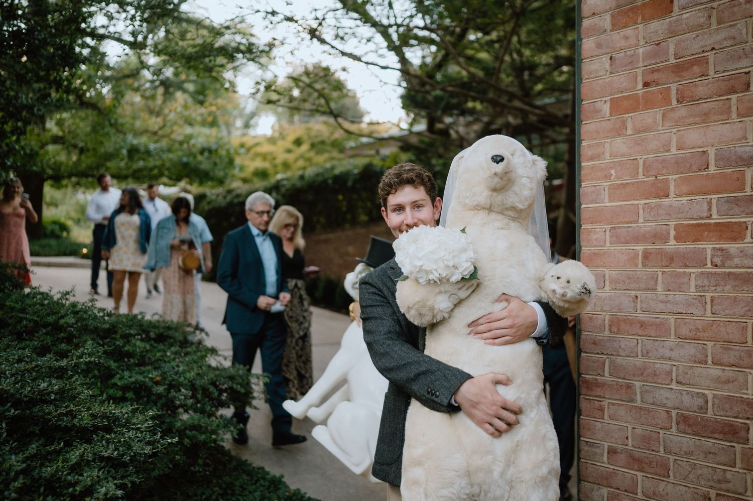 Wedding celebration moment with large teddy bear outside brick building.