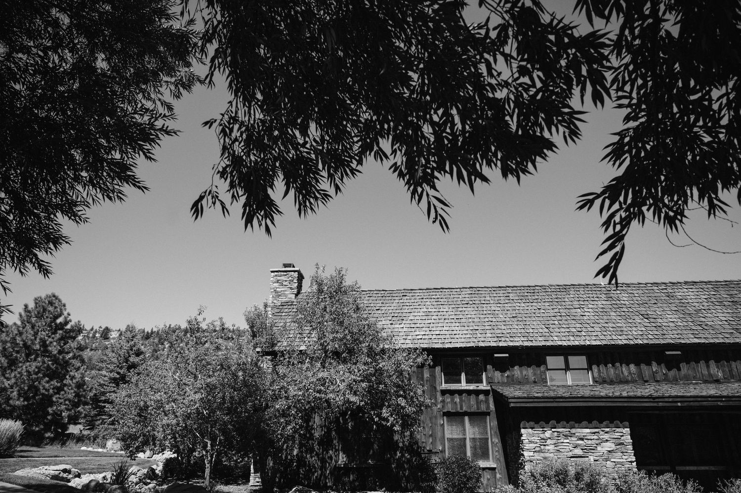 Black and white photograph of a rustic house with trees framing the roof.