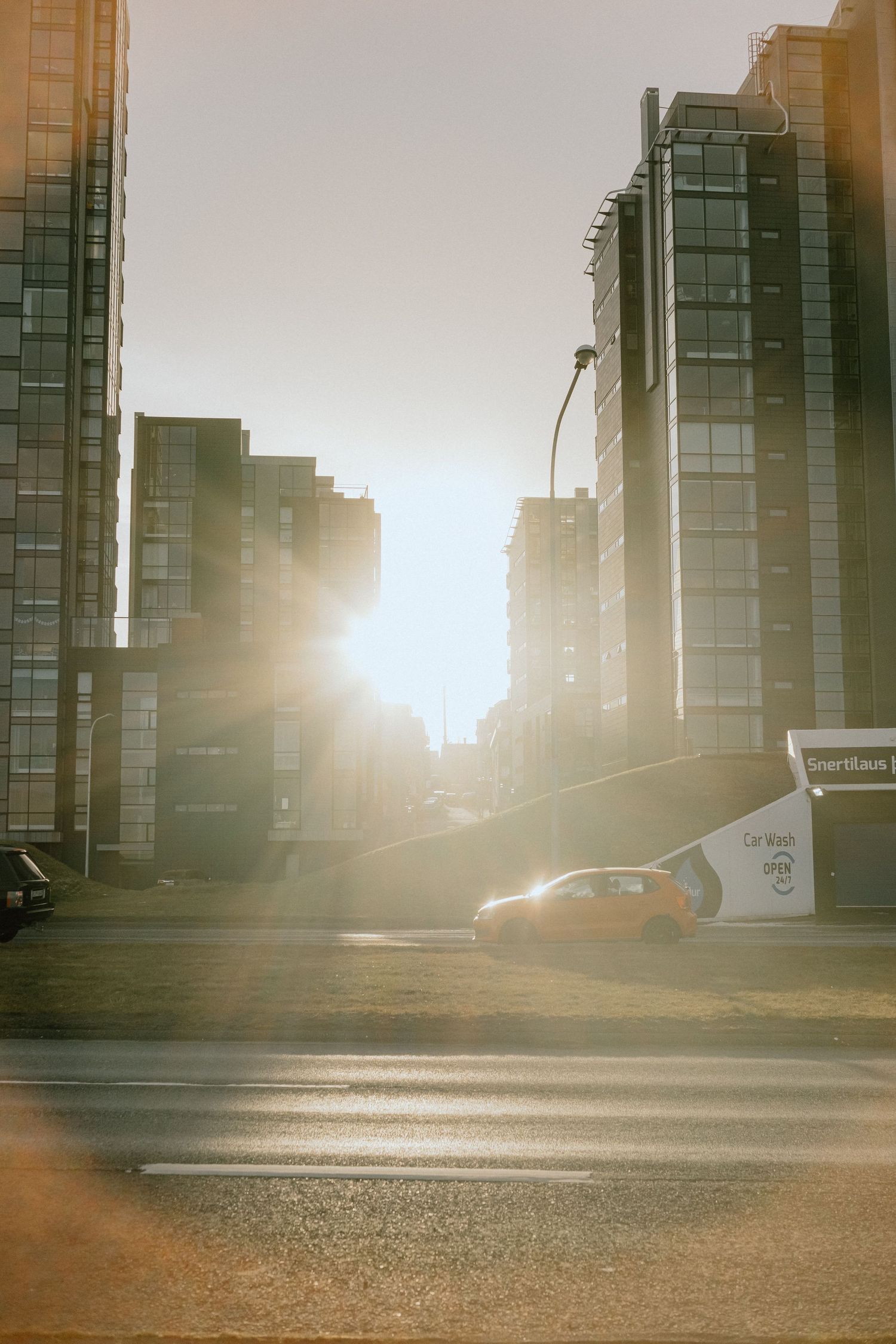 Sunlight streams between modern urban buildings creating dramatic lighting on a city street.