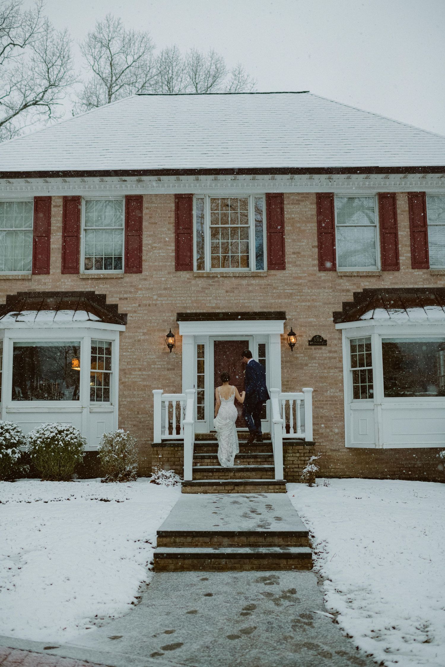 A brick house with white trim and steps covered in snow during winter.
